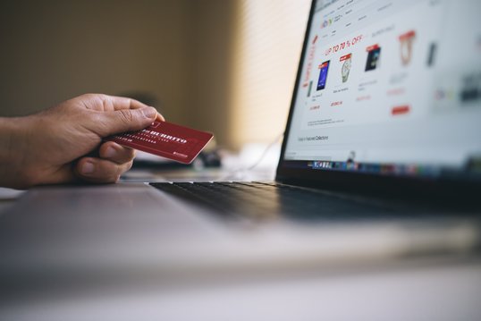 A person is in front of his computer, on an e-commerce site, holding a credit card without in hand.